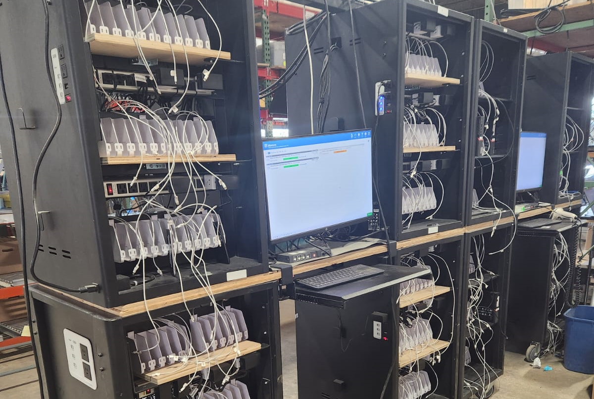 Data wiping setup with racks of IT devices connected to monitors in an ITAD facility