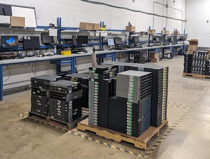 ITAD facility with multiple workstations and pallets of IT equipment, including servers, ready for testing and auditing
